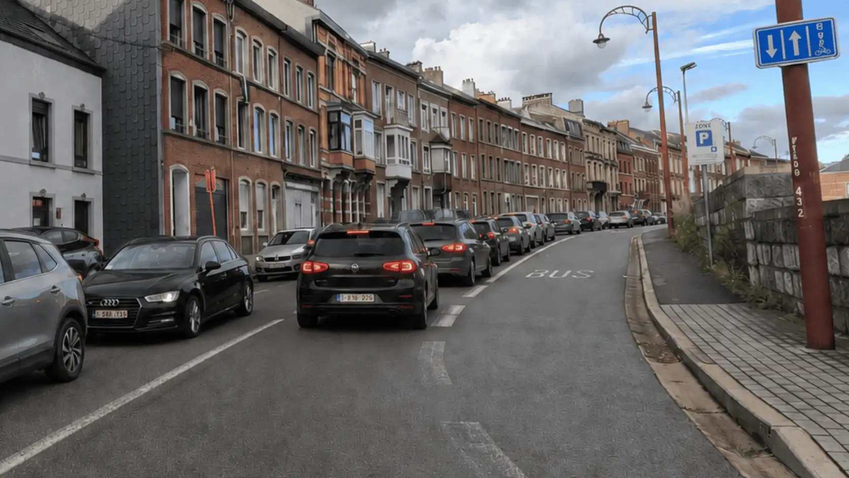 Une file de voitures longe une bande « BUS » libre à droite, séparée par une ligne blanche discontinue ; le panneau BUS comporte aussi un pictogramme de vélo.