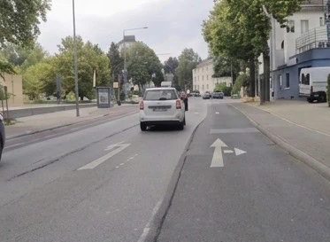 Chaussée bordée de trottoirs, avec une voiture et une flèche au sol indiquant tout droit ou à droite.