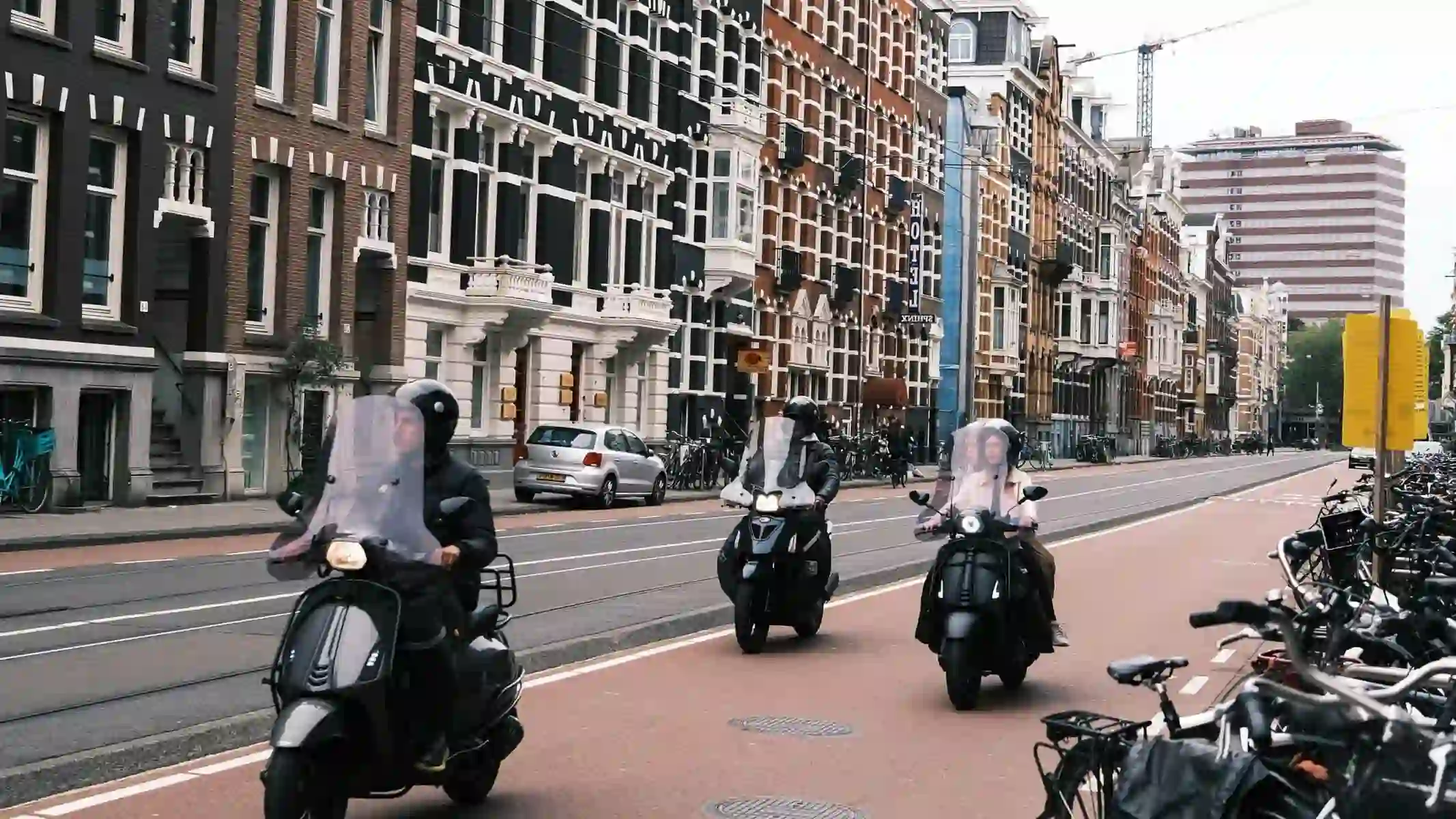 Trois conducteurs casqués à scooter, à différentes distances les uns des autres, dans une rue avec des rails de tram.