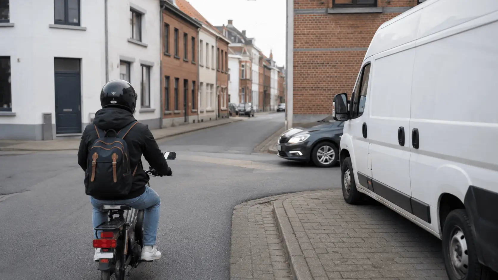 Un cyclomotoriste approche d’un carrefour ; à droite, une camionnette stationnée masque en partie une voiture qui débouche.