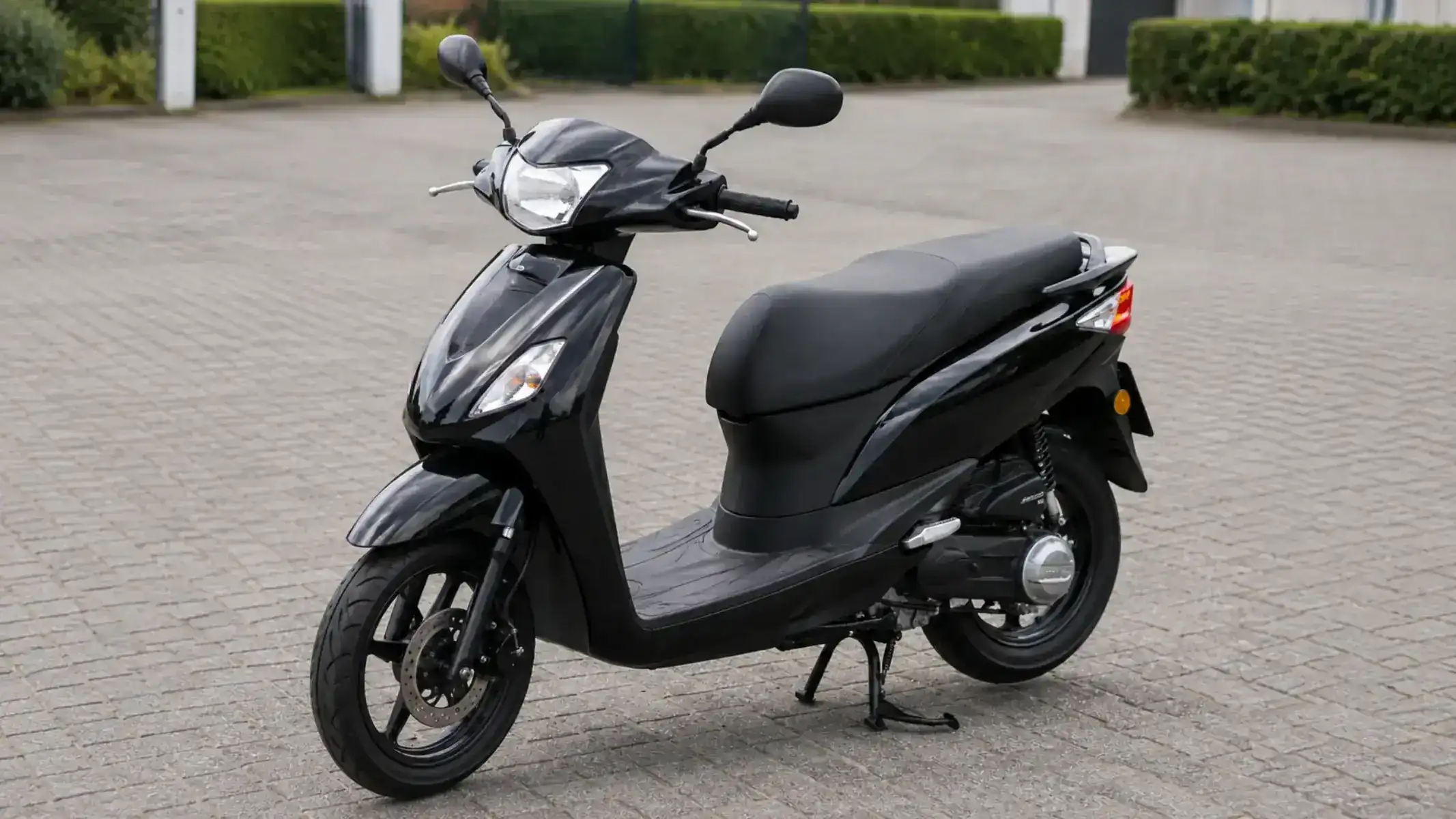 Scooter noir sur sa béquille centrale, vu de trois quarts, avec les pneus, le frein avant, les feux et les rétroviseurs visibles.