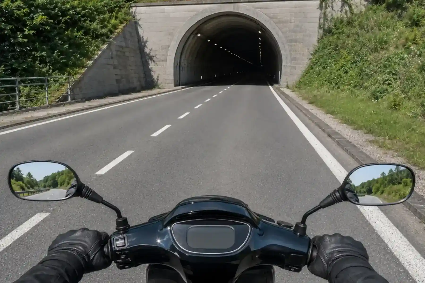 Vue depuis un scooter à l’approche d’un tunnel sombre, en contraste avec la route éclairée par le jour.