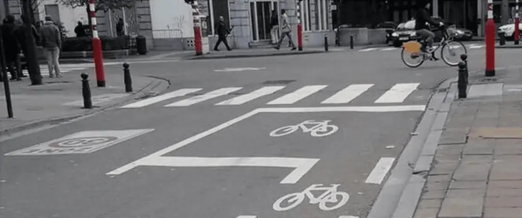 Pictogrammes de vélo, flèche vers la gauche et lignes blanches au sol, avant un passage pour piétons.