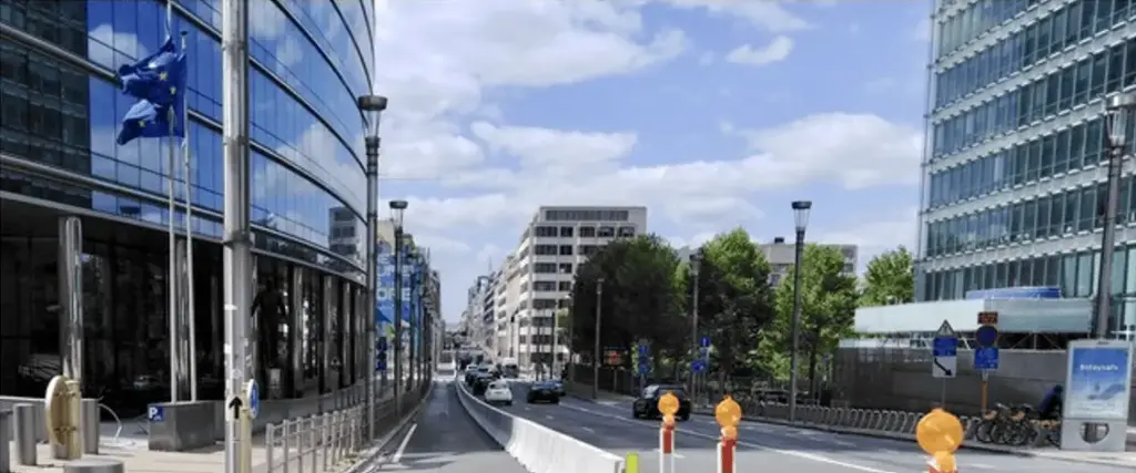 Voitures sur un axe urbain, avec une voie séparée par une barrière en béton et des balises au premier plan.
