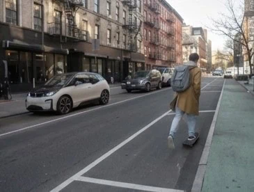 Rue urbaine avec des voitures sur la chaussée et un piéton dans un espace latéral délimité par des lignes blanches.