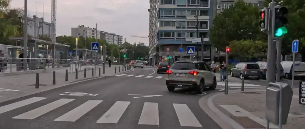 Carrefour avec feu vert pour les véhicules, feux piétons rouges, passages pour piétons et pictogramme de vélo au sol.