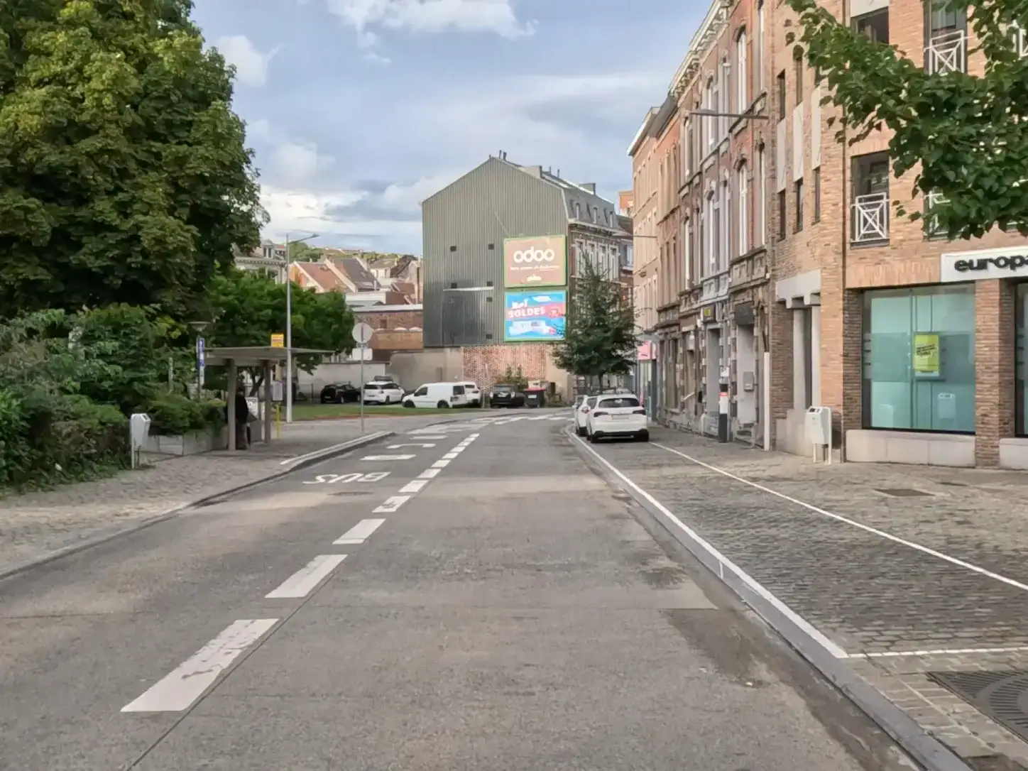 Rue avec une bande « BUS » à gauche, délimitée par une ligne blanche discontinue, et des places de stationnement à droite.
