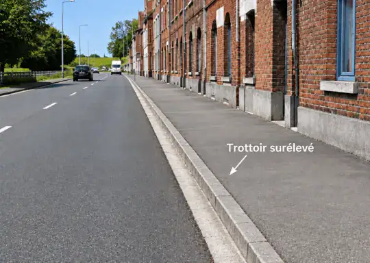 Trottoir surélevé longeant les façades, séparé de la chaussée par une bordure.