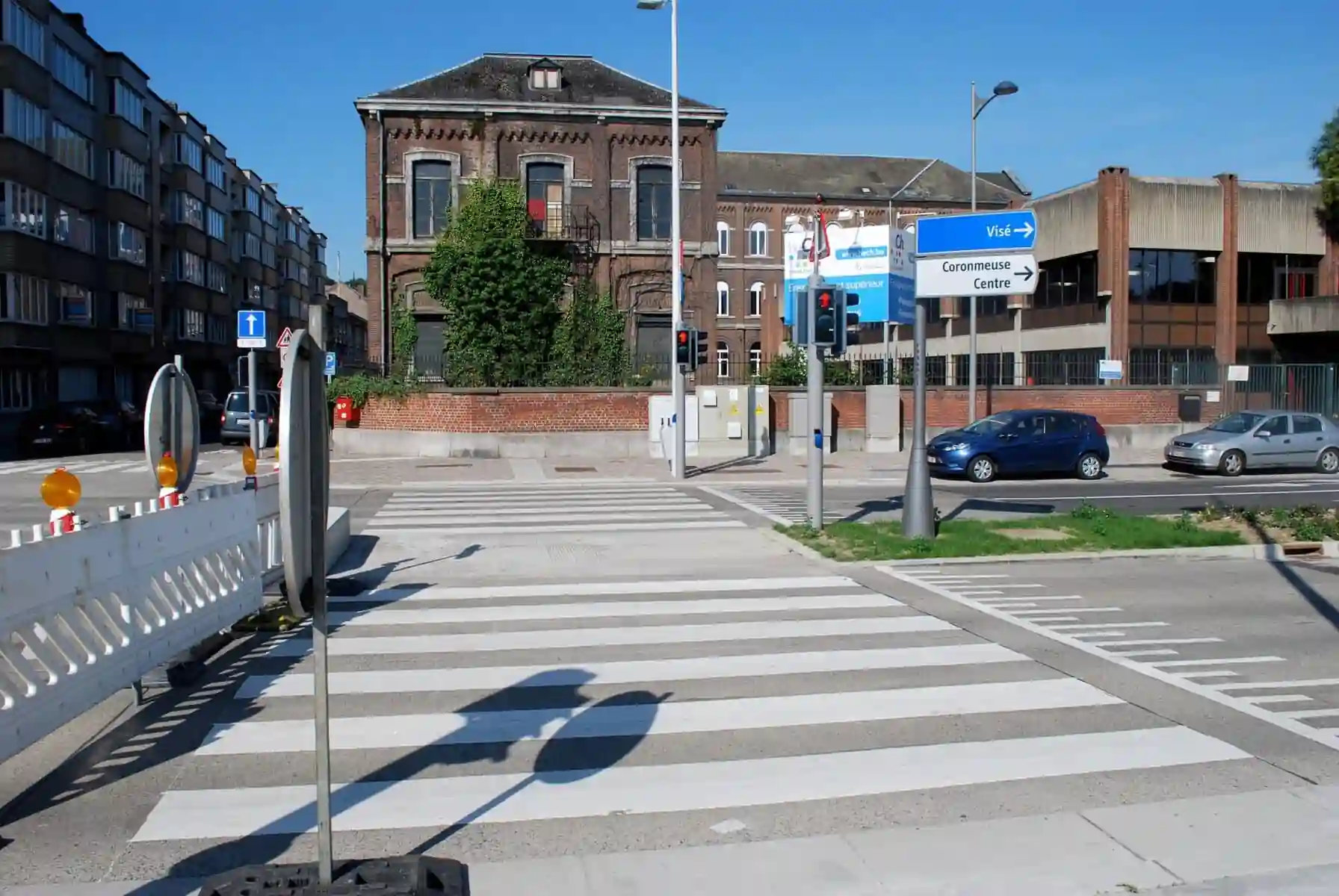 Carrefour avec plusieurs passages pour piétons et des têtes de feux orientées dans différentes directions ; deux silhouettes rouges de piétons sont visibles de face.