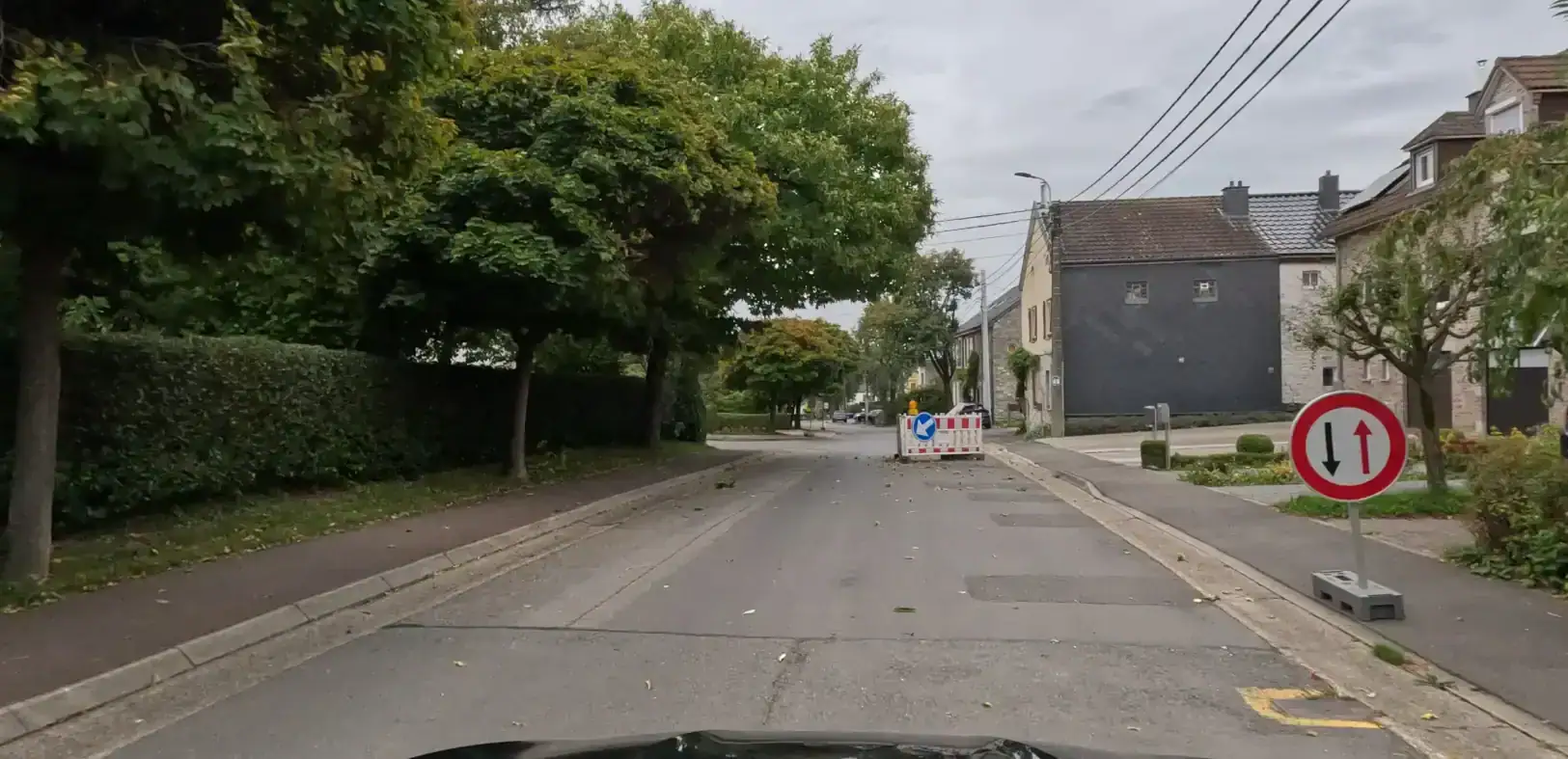 Barrière de chantier à droite avec une flèche blanche sur fond bleu dirigée vers le bas à gauche ; panneau à bord rouge avec une flèche rouge vers le haut et une flèche noire vers le bas.