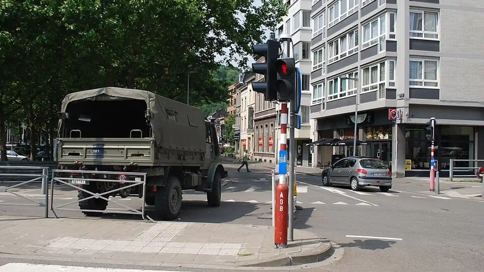 Carrefour avec un camion à gauche, une voiture à droite, un piéton traversant au fond et plusieurs feux de circulation.