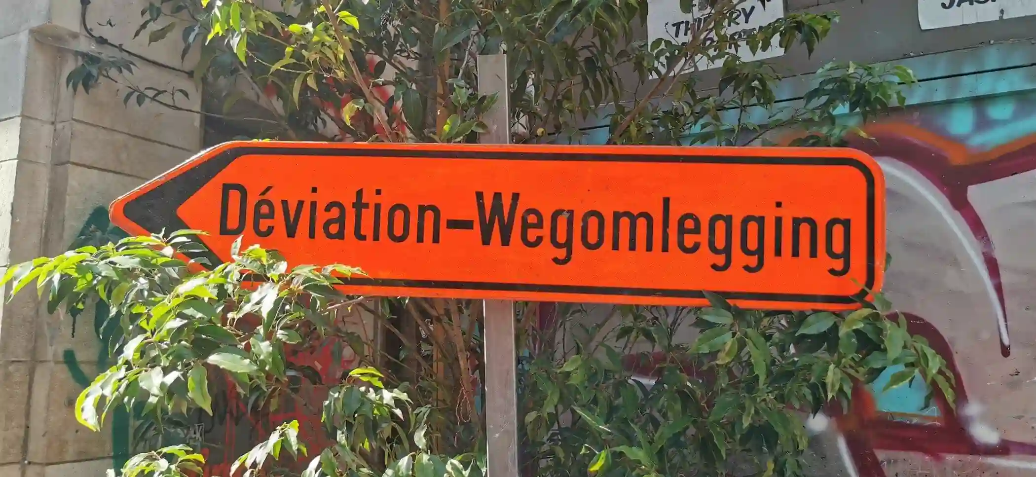 Panneau orange « Déviation – Wegomlegging » en forme de flèche pointant vers la gauche.
