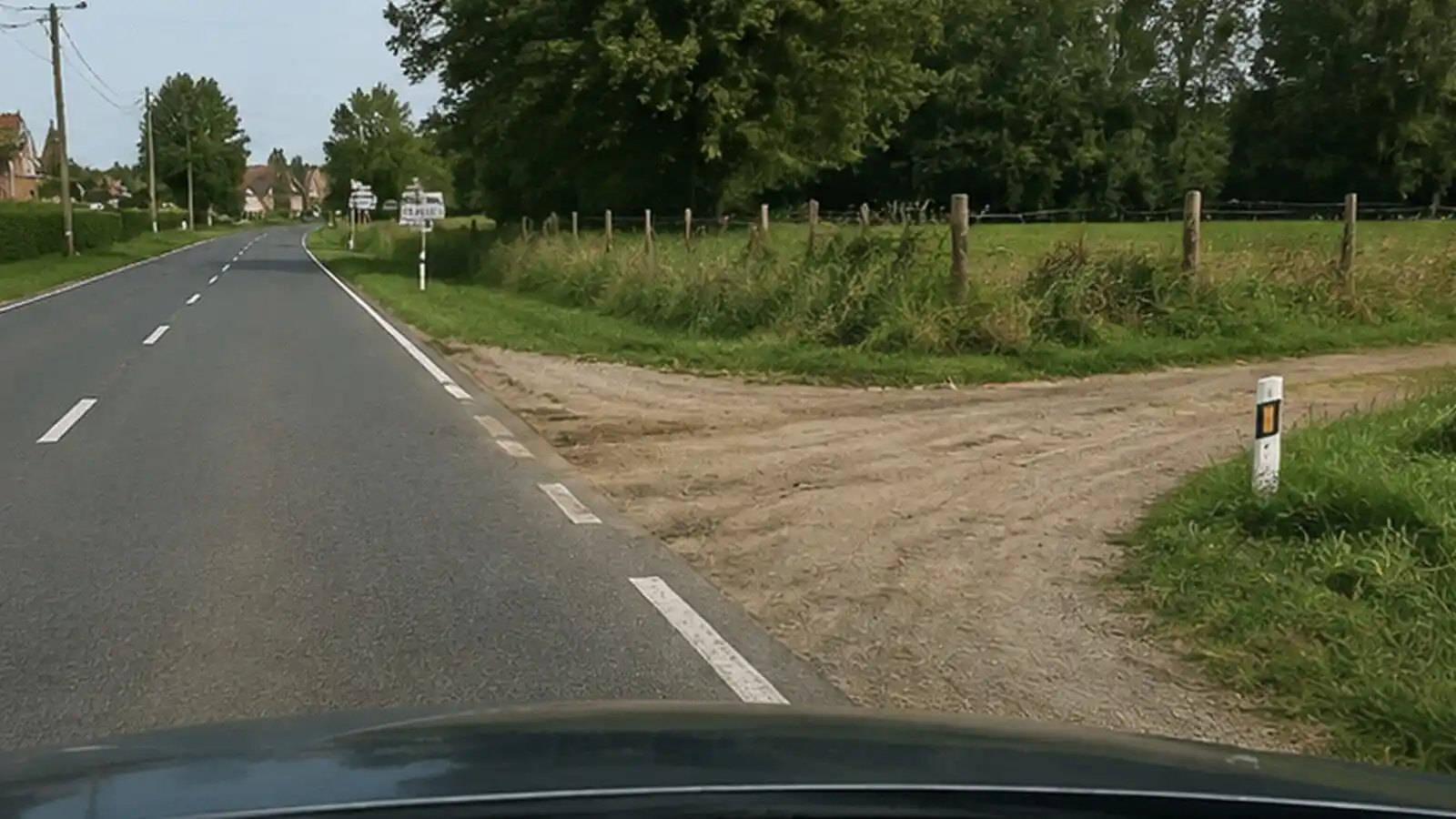 Accès non revêtu rejoignant la chaussée sur la droite, à hauteur d’une interruption de la ligne de rive.