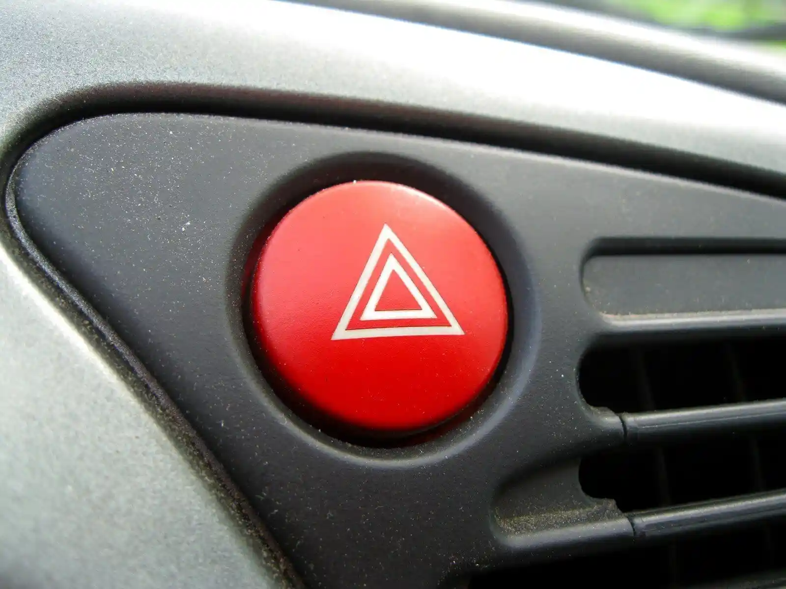Bouton rond rouge des feux de détresse, marqué de deux triangles blancs emboîtés.
