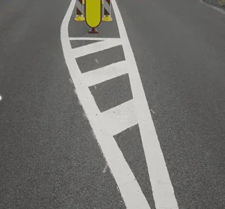 Îlot allongé délimité par des lignes blanches, avec des stries obliques et une balise jaune à son extrémité