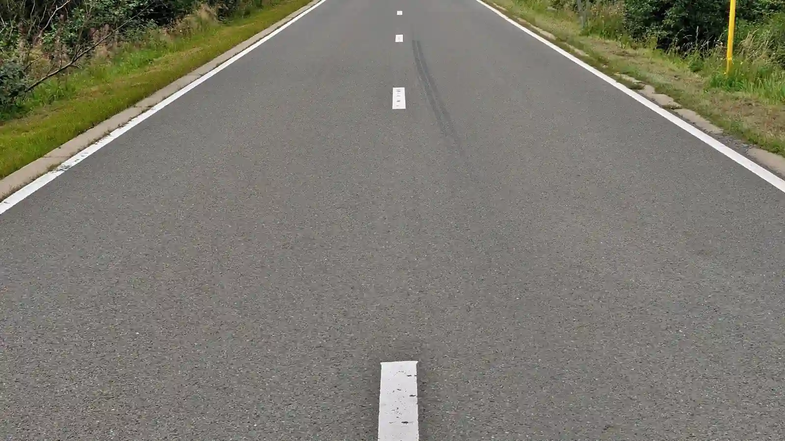 Chaussée unique avec une ligne blanche discontinue au centre et des lignes blanches continues sur les bords, sans séparation physique centrale.