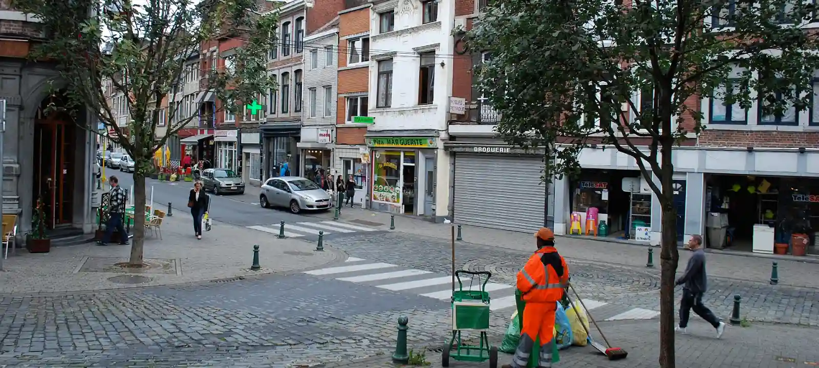 Carrefour urbain pavé, avec passages pour piétons et rues bordées de commerces, sans signal de priorité visible.