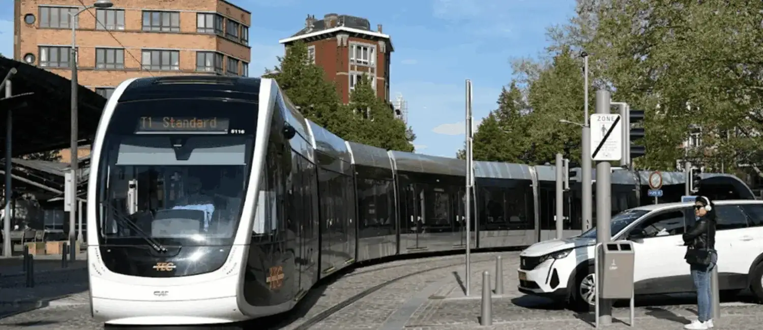 Tram sur des rails en courbe, avec une voiture blanche à droite, près de la voie ferrée.
