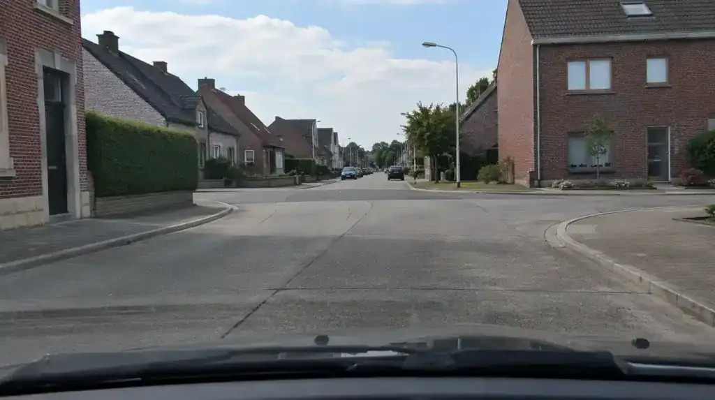 Carrefour dans une rue bordée de maisons et de trottoirs, avec des véhicules stationnés plus loin.