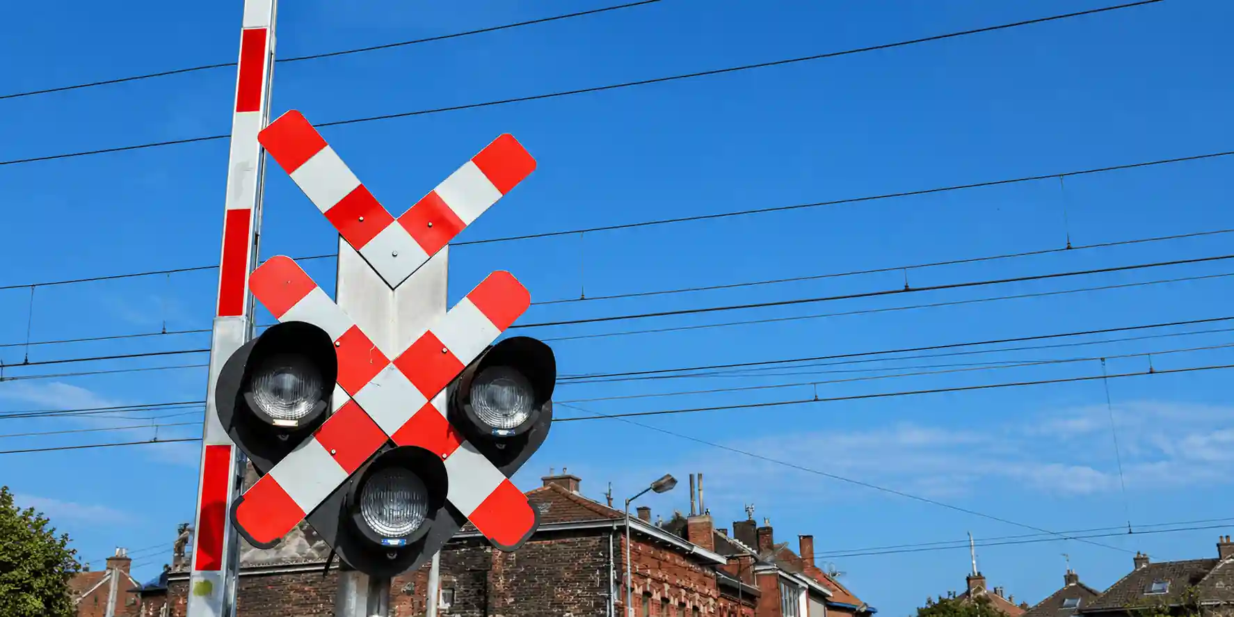 Signal de passage à niveau avec trois optiques disposées en triangle, sous une double croix de Saint-André, et une barrière relevée.