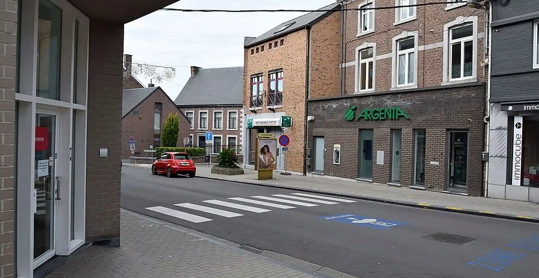 Passage pour piétons, traits jaunes discontinus sur la bordure opposée et signal bleu à flèche blanche dans une rue commerçante.