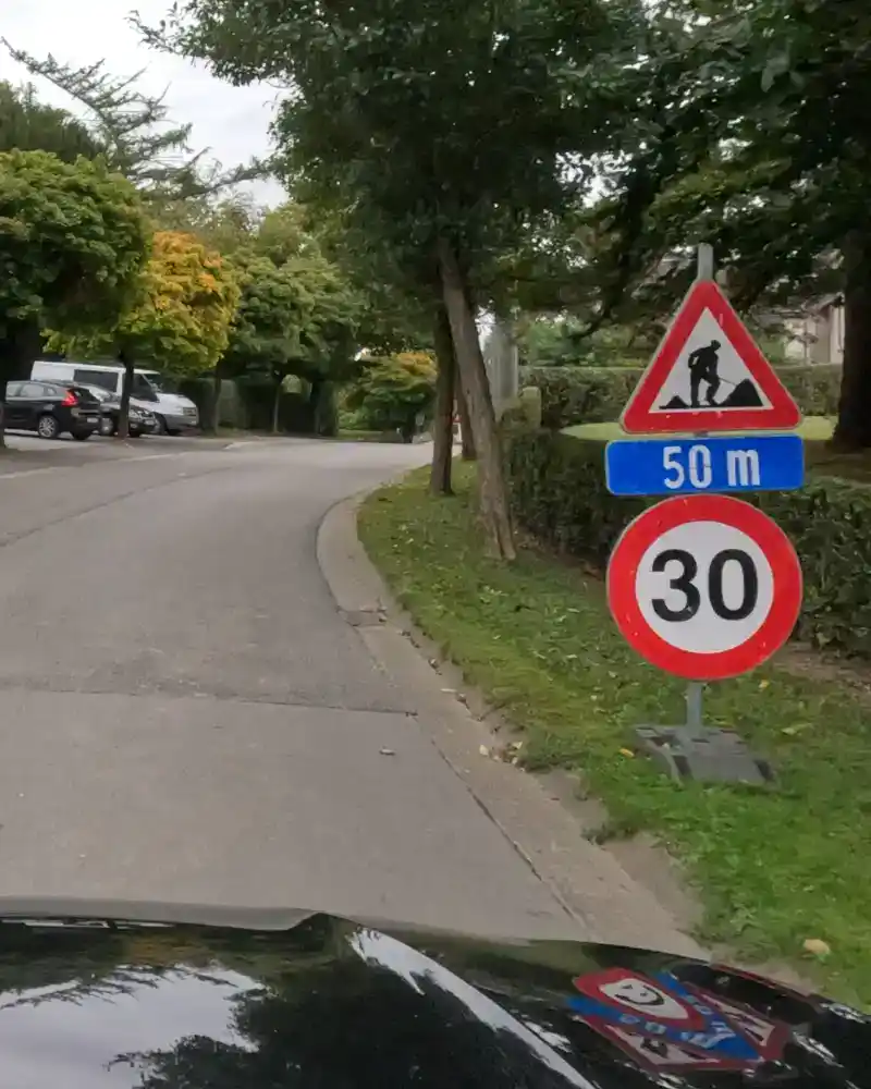 Signal de travaux avec panneau additionnel « 50 m » et signal de limitation à 30 km/h au bord de la route.