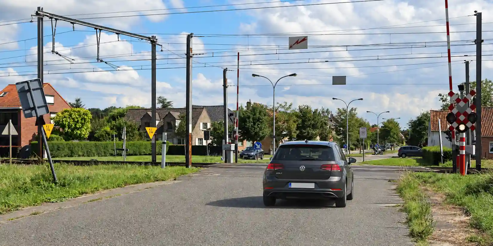 Voiture devant un passage à niveau, avec les barrières levées et un feu blanc allumé à droite.