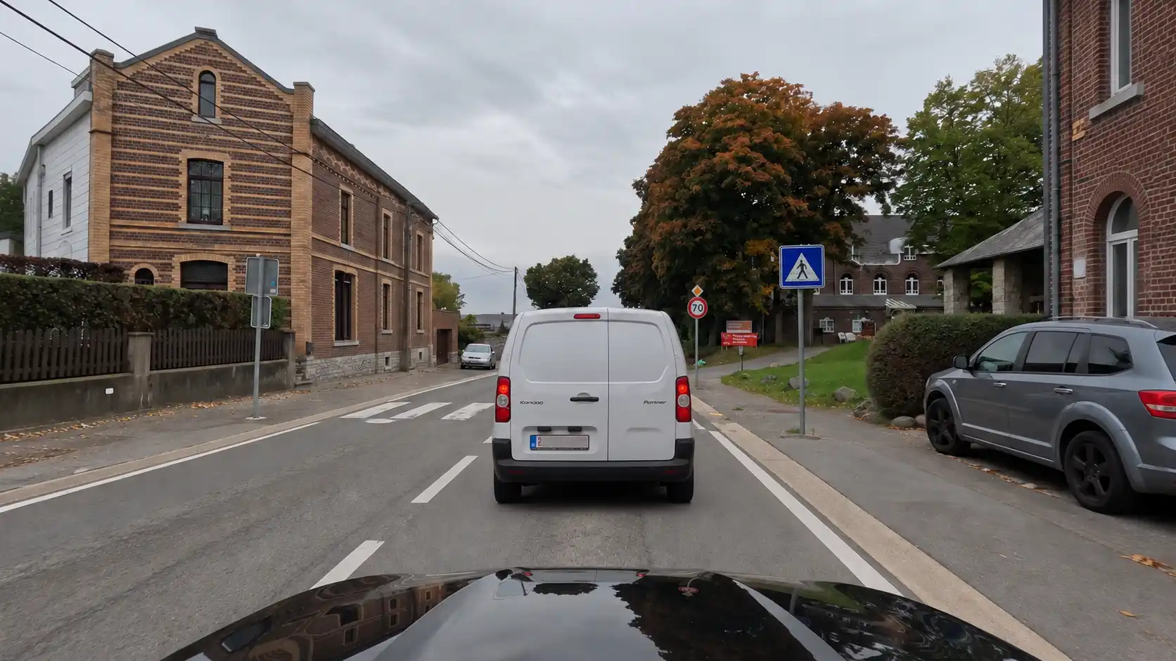Camionnette masquant une partie d’un passage pour piétons, signalé par un panneau bleu à droite.