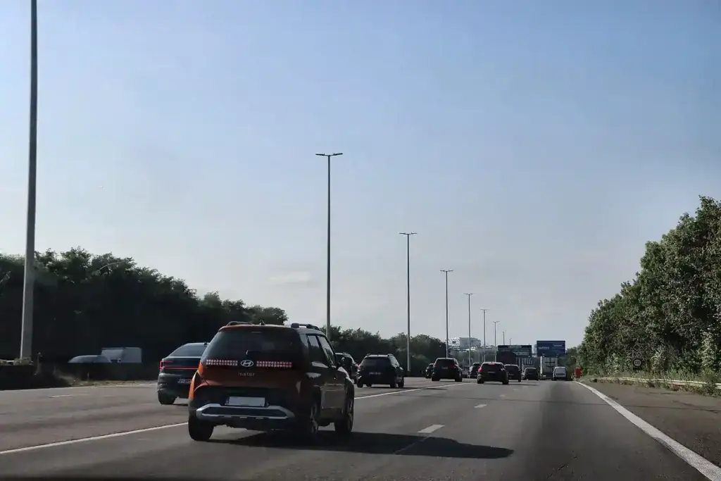 Vue depuis la bande de droite d’une chaussée à quatre bandes : voitures sur les bandes de gauche et du milieu, plusieurs véhicules plus loin, panneaux directionnels au loin et ligne blanche continue à droite.