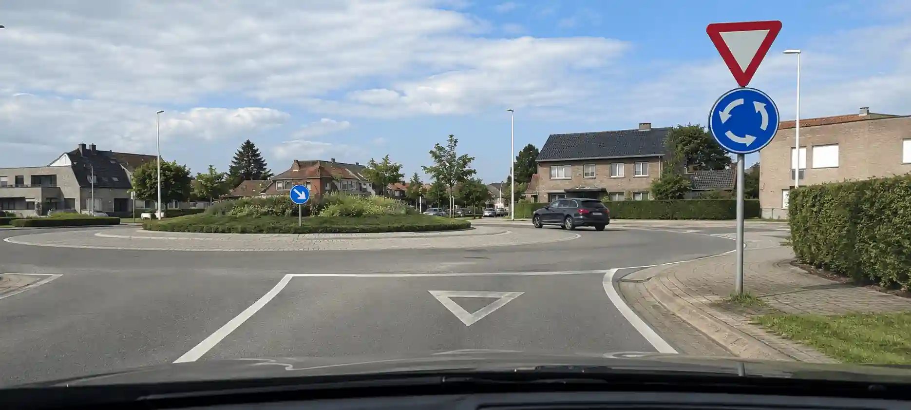 Vue depuis une voiture à l’entrée d’un rond-point : le signal B1 surmonte le D5 à droite, tandis qu’une voiture circule déjà dans l’anneau.