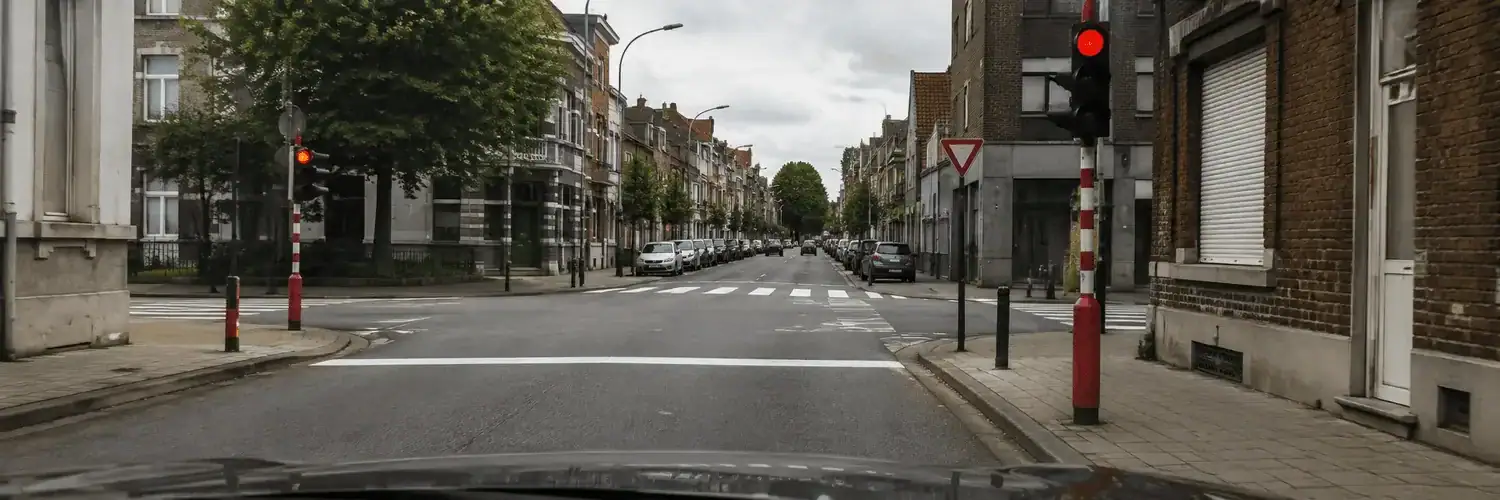 Vue depuis une voiture : feu rouge à droite et ligne d’arrêt blanche continue en travers de la chaussée avant le carrefour.