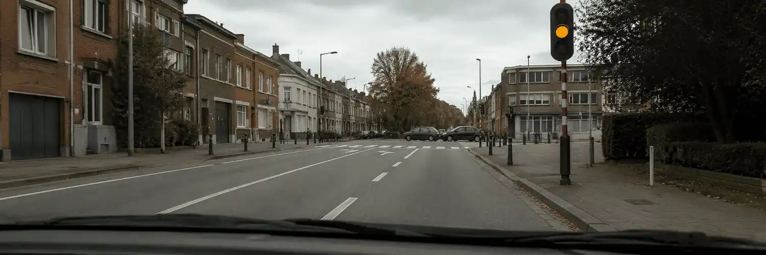 Vue depuis une voiture : feu jaune-orange allumé à droite, avant un carrefour avec passage pour piétons.