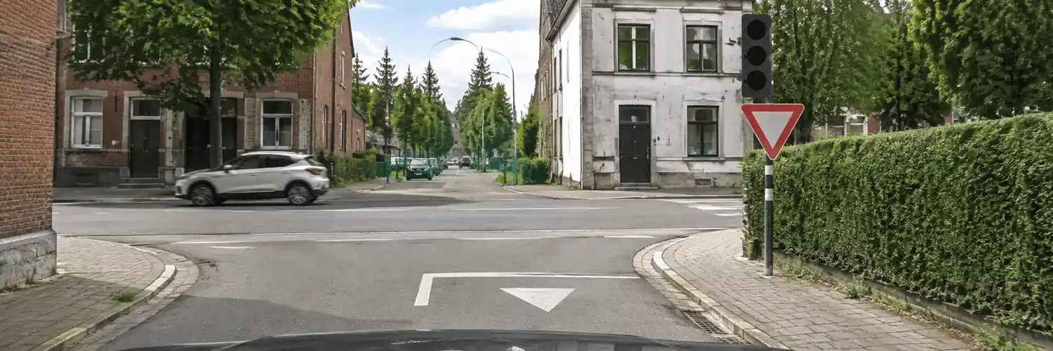Feu tricolore éteint au-dessus d’un panneau triangulaire inversé à bord rouge ; un triangle blanc est peint au sol avant le carrefour.