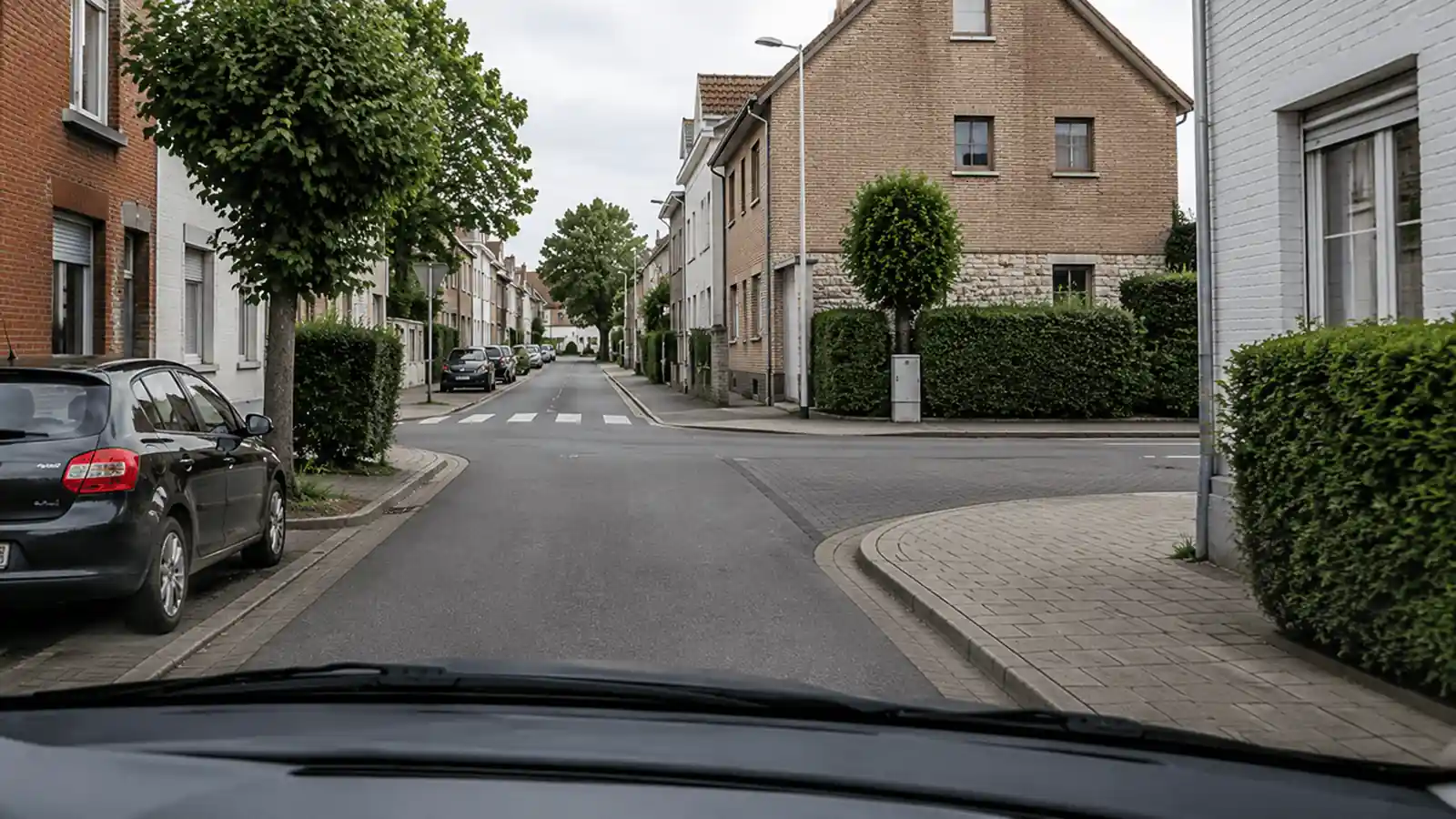 Carrefour résidentiel momentanément vide, avec des trottoirs, un passage pour piétons en face et une voiture stationnée à gauche.