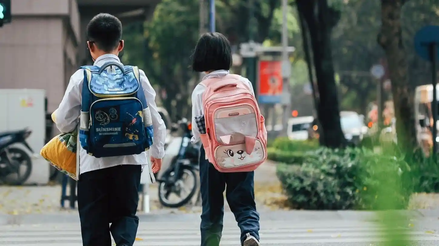 Deux enfants portant des cartables, vus de dos, traversent la chaussée sur un passage pour piétons.