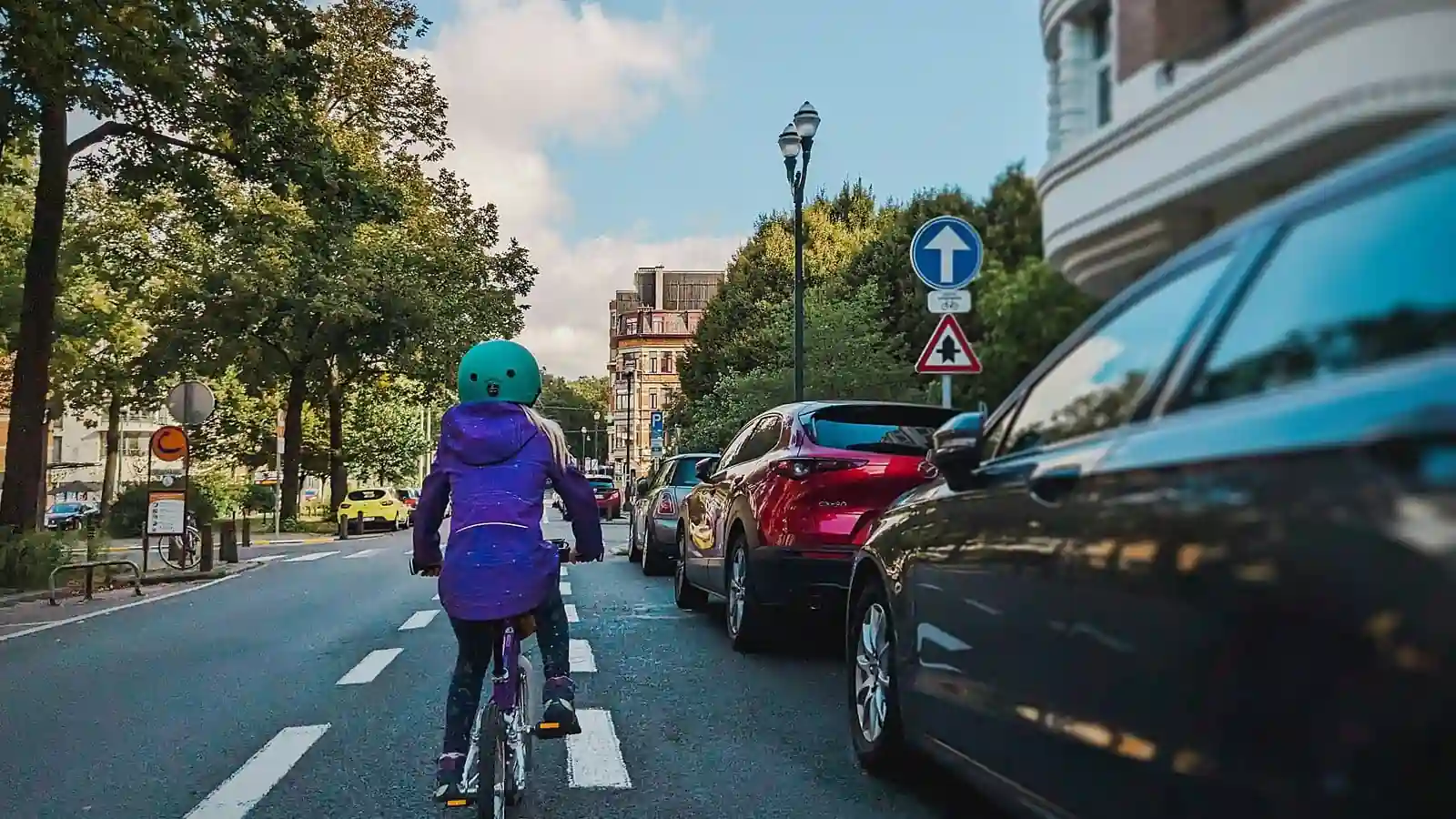 Une cycliste vue de dos longe de près une rangée de voitures stationnées à sa droite.