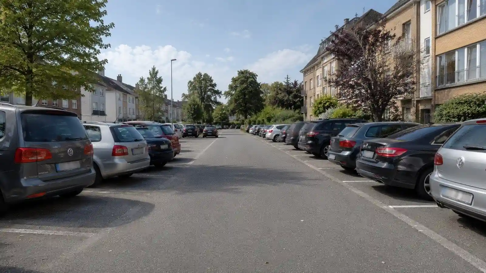 Allée de parking entre deux rangées de voitures stationnées, sans piéton visible.