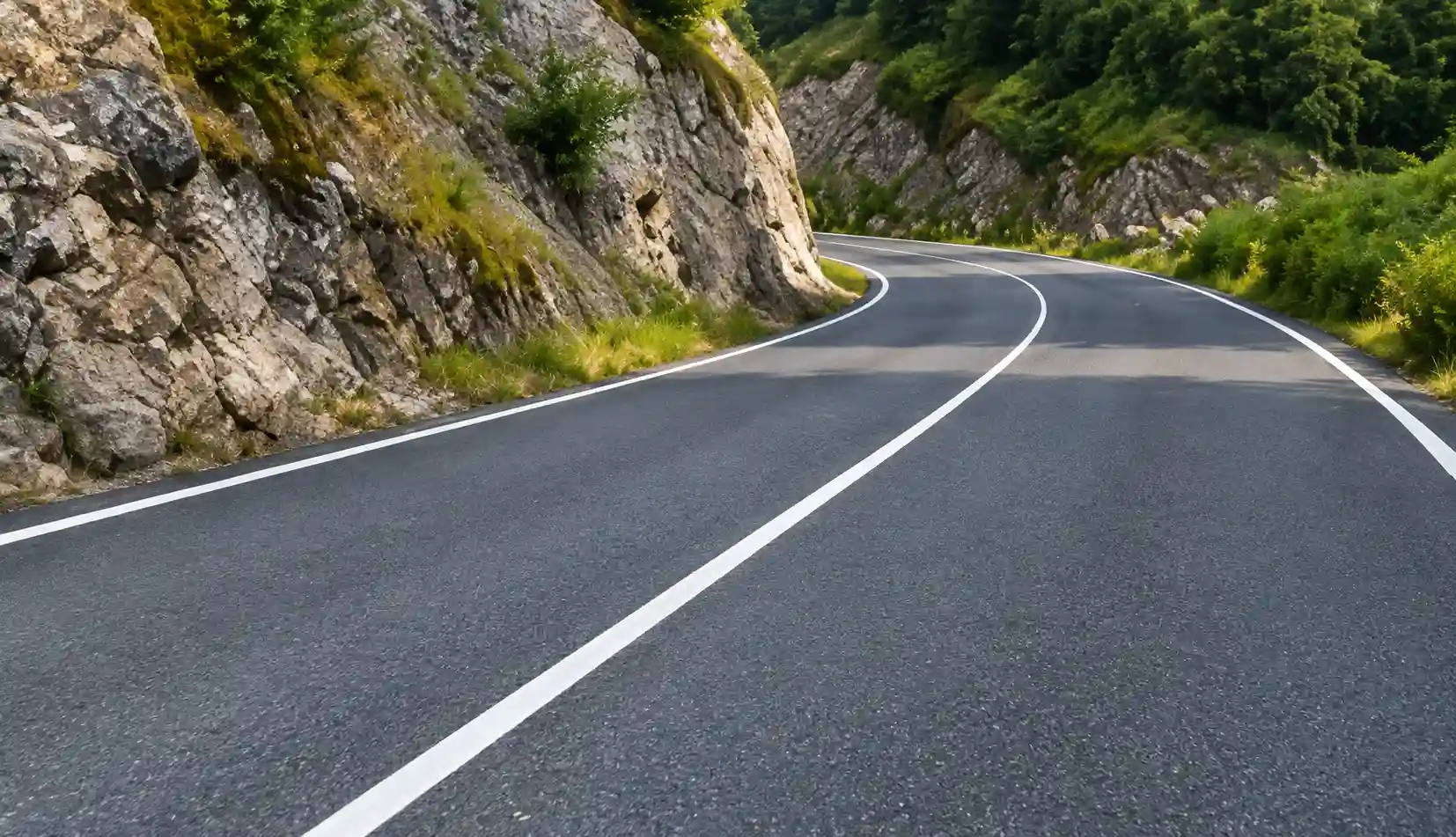Route en virage, avec une ligne centrale continue et une paroi rocheuse masquant la suite de la chaussée.