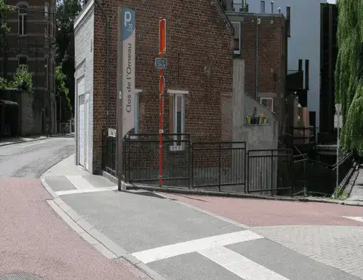 Trottoir se prolongeant à travers un accès latéral, avec un revêtement gris distinct des surfaces voisines.