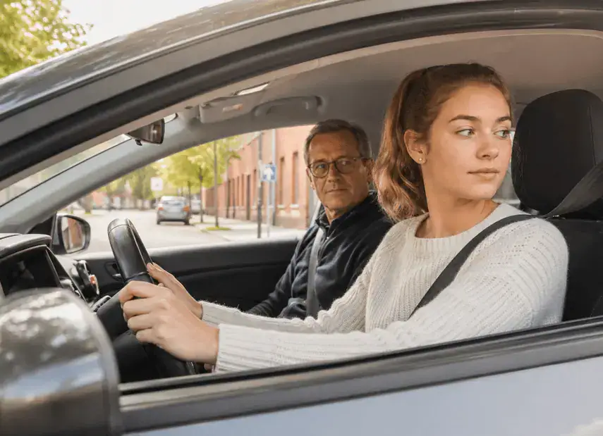 Conductrice portant sa ceinture de sécurité, les mains sur le volant, tournant la tête pour regarder derrière elle.