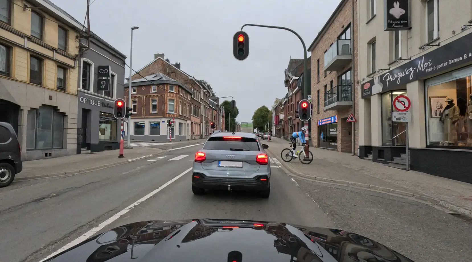 Voiture devant un passage pour piétons à un carrefour où les feux sont rouges, avec un cycliste sur le trottoir à droite.