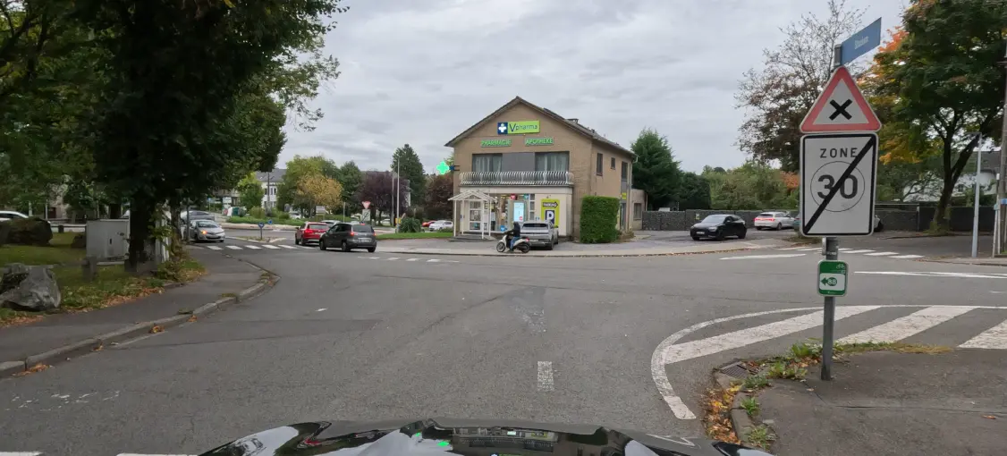 À droite du carrefour, un panneau rectangulaire « ZONE 30 » grisé et barré d’une diagonale noire se trouve sous un triangle portant une croix noire.