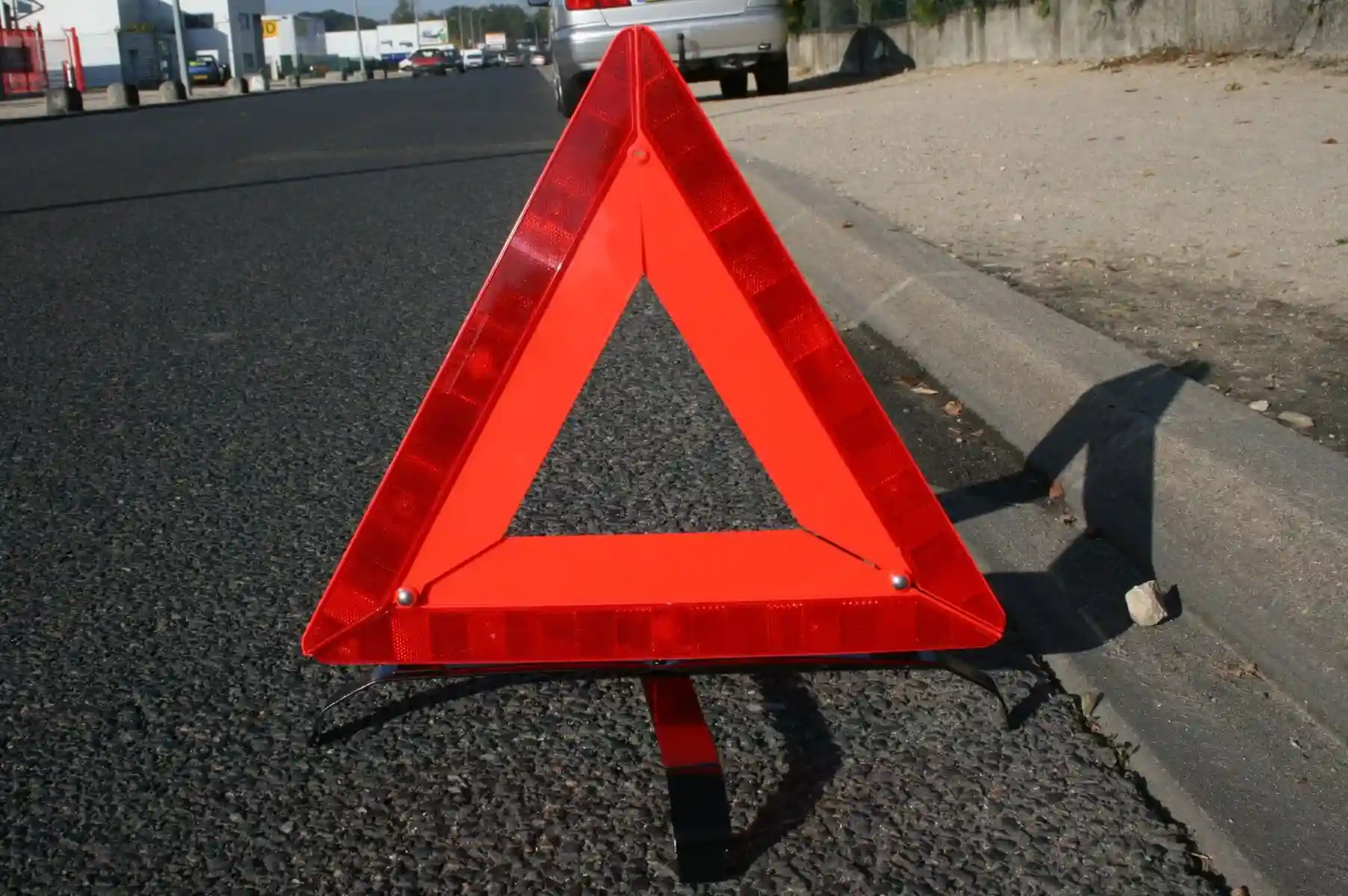Triangle de danger rouge posé verticalement au bord de la chaussée, près d’un trottoir.
