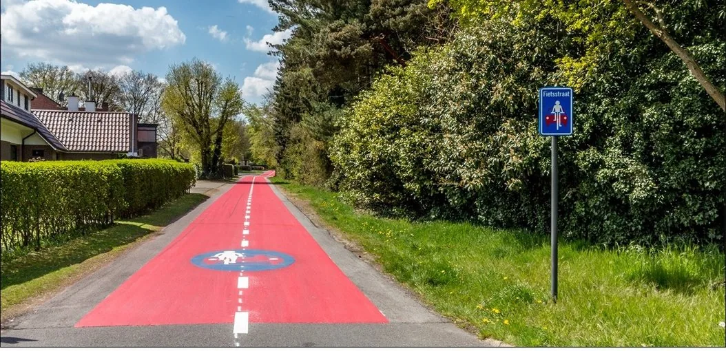 Rue à revêtement rouge à Genk, avec pictogrammes au sol et ancien signal F111 « Fietsstraat » à droite.
