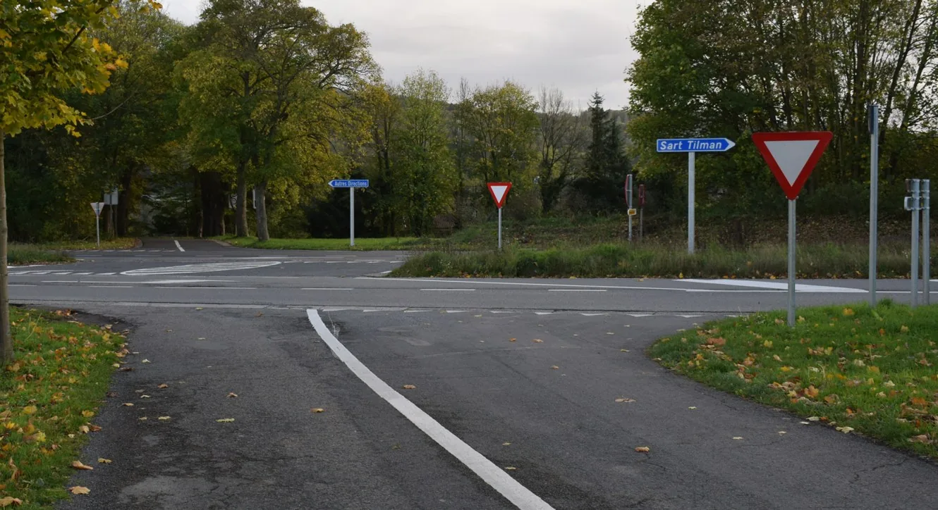Approche d’un carrefour : à droite, un triangle blanc bordé de rouge, pointe vers le bas, fait face au conducteur. La voie transversale est visible devant lui.