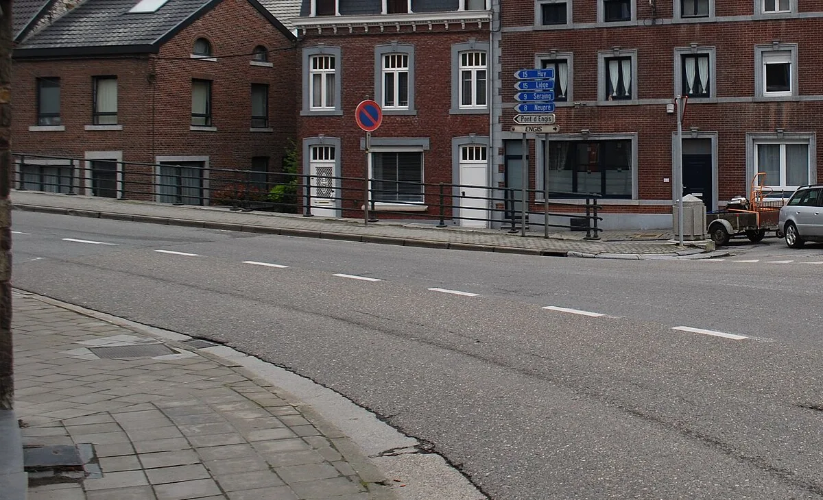 Le bord proche de la chaussée apparaît au premier plan. Un signal E1 est placé sur le trottoir opposé.