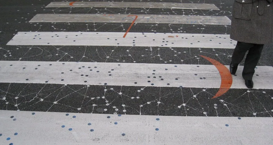Une personne, partiellement visible à droite, marche sur les bandes blanches d’un passage piéton décoré de motifs colorés.