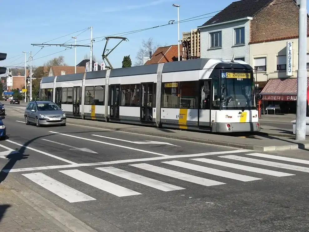 À Melle, tram à quai, voiture venant vers l’observateur et passage piéton au premier plan. Le tram est à gauche du conducteur de la voiture ; un équipement lumineux est partiellement hors cadre à gauche.