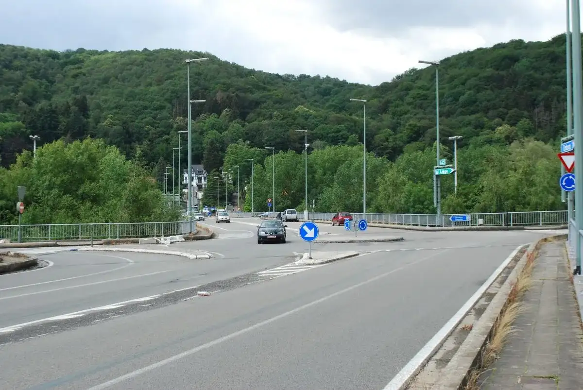 Îlot à Liège, avec un triangle sur pointe et un disque bleu à trois flèches circulaires sur l’entrée à droite ; une voiture circule autour de l’îlot.