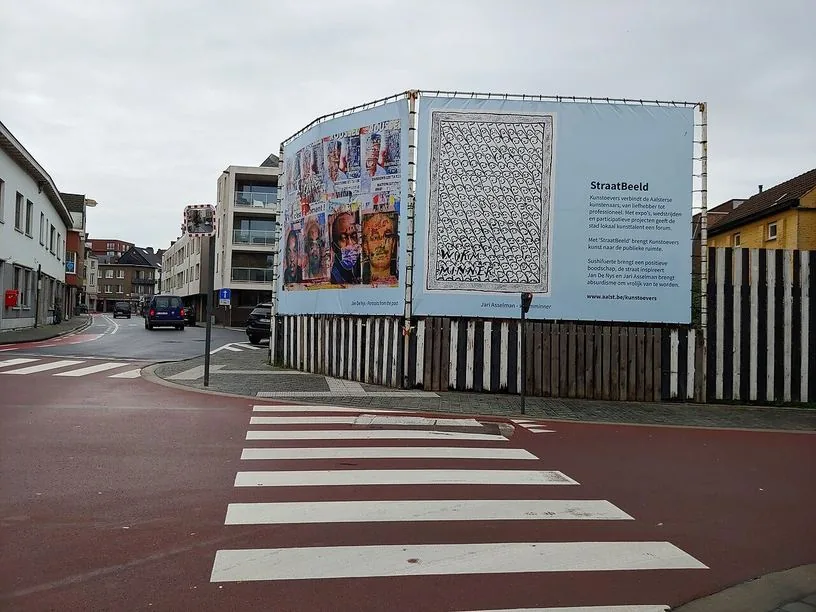 Passage piéton à bandes blanches sur une chaussée rouge, près d’un carrefour à Aalst ; aucun piéton visible sur les bandes.